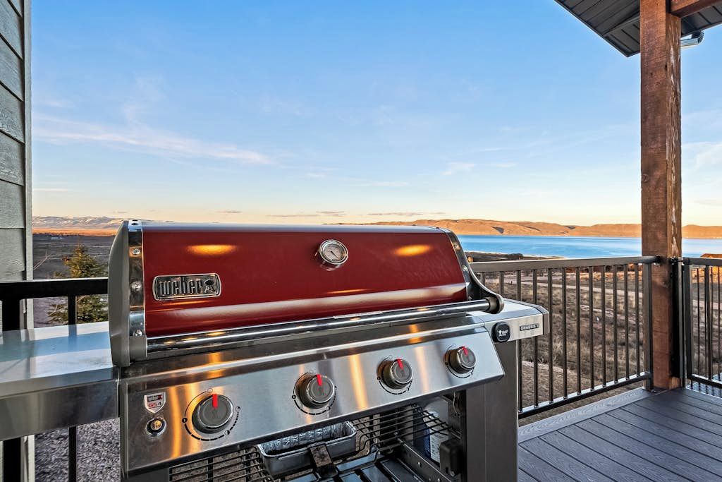 A Weber gas grill on an outdoor deck with a view of a lake and mountains.
