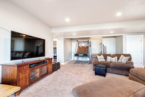 A living room with a flat-screen TV, a brown sofa, and a wooden entertainment center. - Two Bear Lodge - Sleeps 40, Pools & Beach Access (Fish Haven)