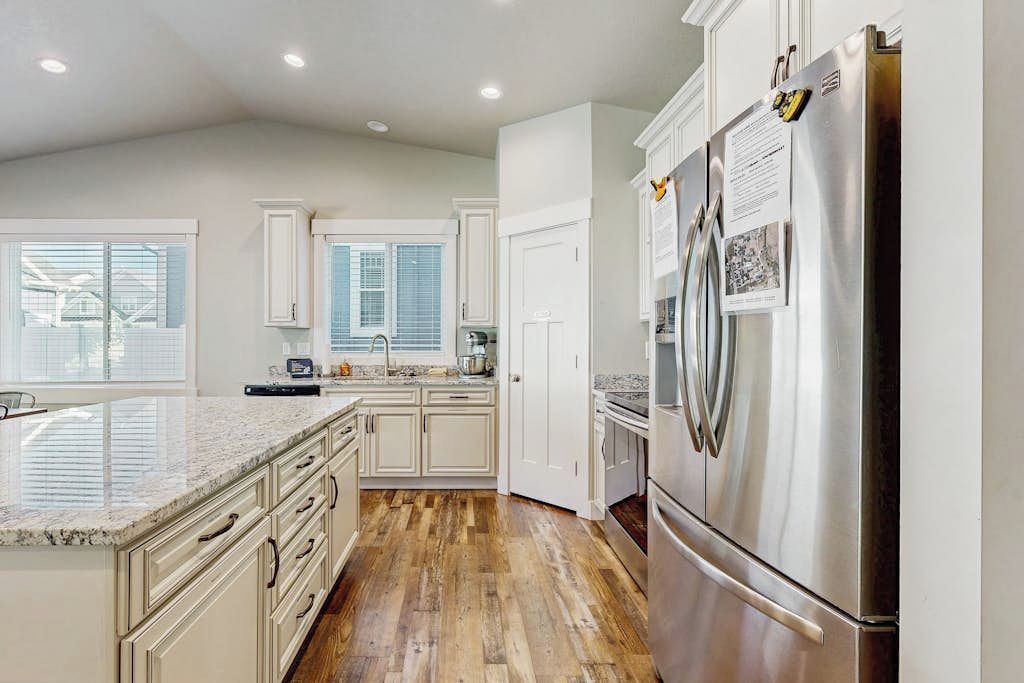 A kitchen with white cabinets, a stainless steel refrigerator, and a wooden floor.