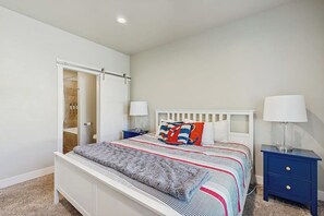 Een slaapkamer met een bed, twee nachtkastjes, een kledingkast met schuifdeur en een zichtbare badkamer door de deur.
