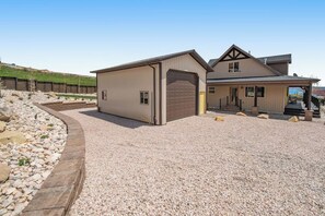 A two-story building with a garage, a covered porch, and a gravel driveway. - Cubbyz Cabin - Lake Views, Hot Tub, Near Marina (Garden City)
