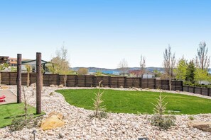 A landscaped backyard with a wooden fence, a grassy area, and a small tree. - Cubbyz Cabin - Lake Views, Hot Tub, Near Marina (Garden City)