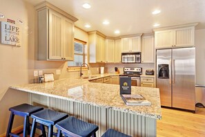 A modern kitchen with granite countertops, stainless steel appliances, and a bar area with stools. - Cubbyz Cabin - Lake Views, Hot Tub, Near Marina (Garden City)