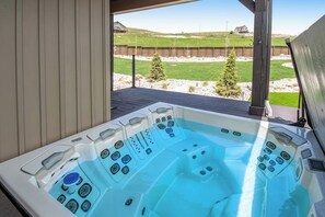 Un jacuzzi con múltiples chorros, una terraza de madera y vistas a un patio cercado con árboles.