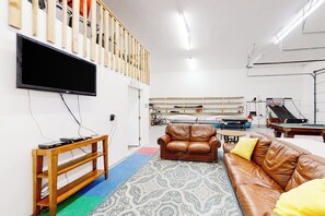A living room with a brown leather sofa, a television mounted on the wall, a pool table, and a wooden staircase. - Kokomo Kottage - Game Room, Fire Pit & Playset (Garden City)