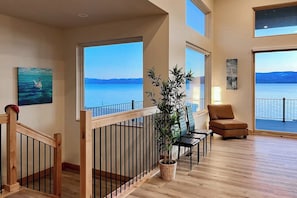 Une pièce spacieuse avec un plancher en bois, un balcon doté d’une balustrade, une plante en pot, un canapé et un tableau accroché au mur.