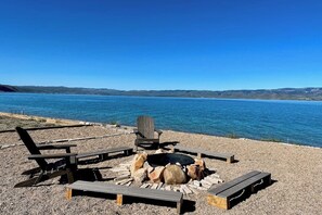 A fire pit with seating around it, overlooking a body of water. - Beachfront Haven - Private Beach, Courts & Views (Laketown)