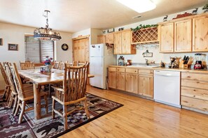 A kitchen with wooden cabinets, a dining table with chairs, a chandelier, and a refrigerator. - Moose Mountain Retreat (Fish Haven)