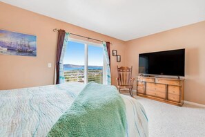 Ein Schlafzimmer mit Bett, Kommode, Fernseher und einem Fenster mit Vorhängen.