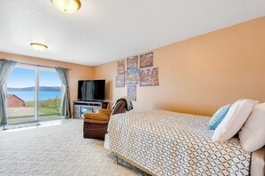 Ein Hotelzimmer mit Bett, Fernseher, Schreibtisch mit Stuhl und Fenster mit Blick auf ein Haus und Wasser.
