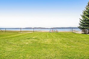 A grassy field with a red metal structure, a clear sky, and distant mountains. - Lollipop Lakehouse - Lakefront & Game Room (Garden City)