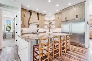 A kitchen with a large island, wooden cabinets, and a stainless steel refrigerator. - Marina View at Daisy Bay (Garden City)