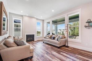 A spacious living room with a fireplace, a sofa, and large windows offering a view of the outdoors. - Marina View at Daisy Bay (Garden City)