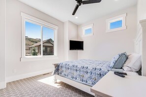 A bedroom with a bed, a television mounted on the wall, and a window with a view of a house. - Marina View at Daisy Bay (Garden City)