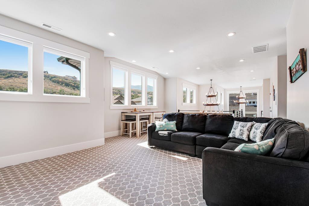 A spacious living area with a large window, a dark-colored sofa, and a patterned carpet.
