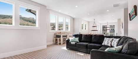 A spacious living area with a large window, a dark-colored sofa, and a patterned carpet.