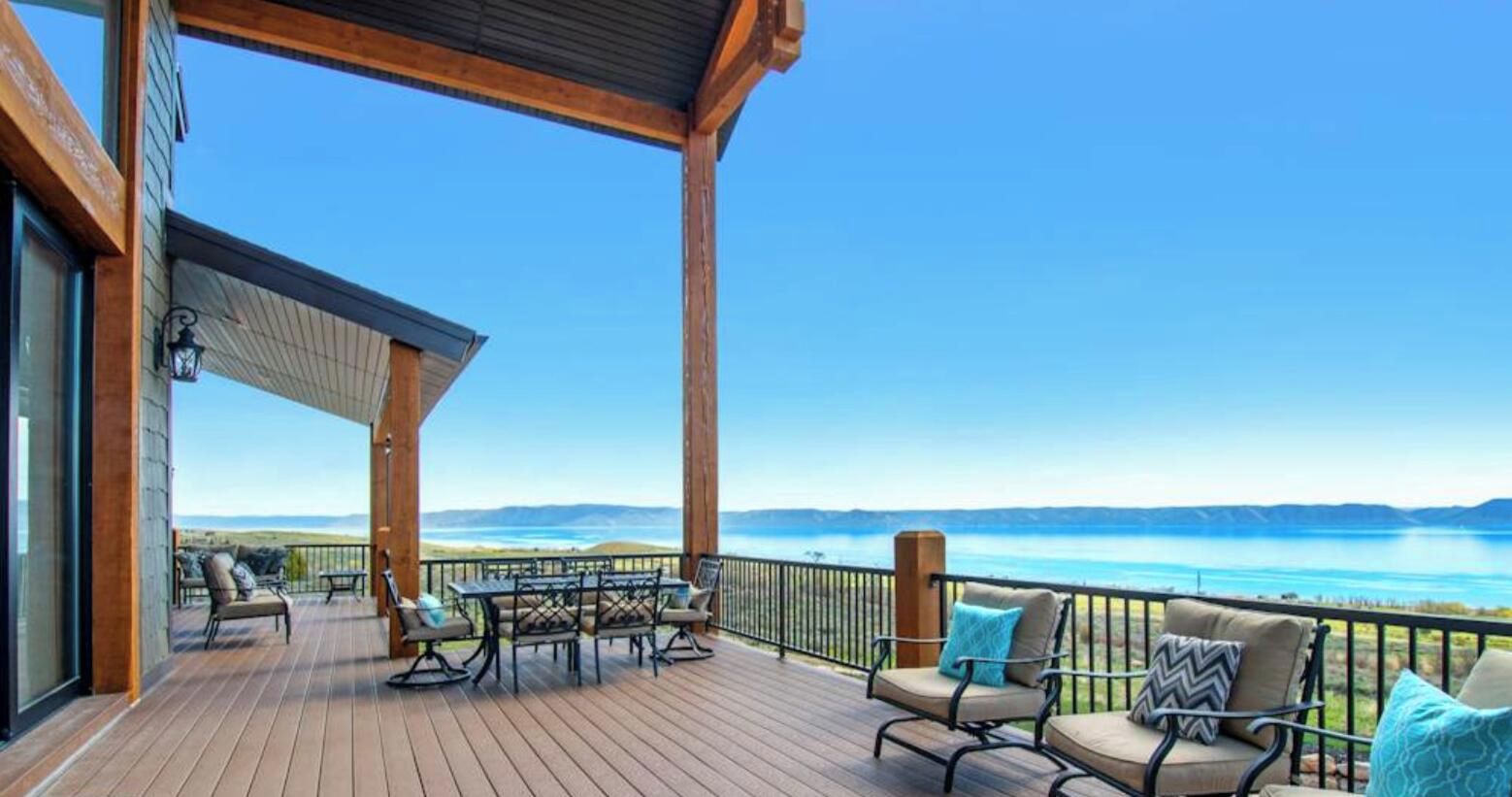 A wooden deck with outdoor furniture, a table, and a view of a lake and mountains.