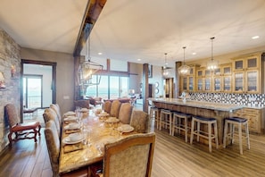 Un vaste espace dédié à la salle à manger, avec une longue table dressée pour le repas, un bar avec des tabourets et une cuisine dotée de meubles en bois.