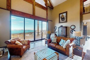 Un salon spacieux doté d’une grande fenêtre donnant sur un balcon, d’un canapé en cuir et d’un pouf à motifs.