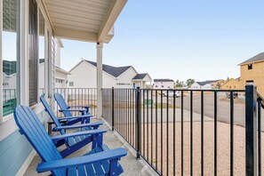 A covered outdoor seating area with blue chairs, a metal fence, and a view of residential buildings in the background. - Grandma Buddy's House (Garden City)
