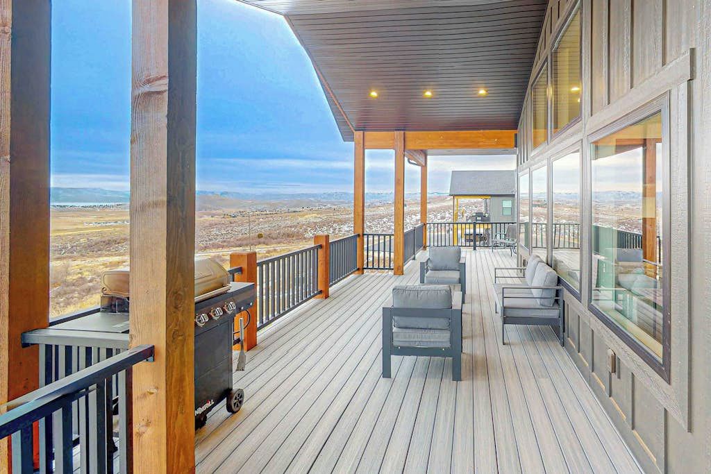 A covered outdoor deck with a grill, seating, and a view of a mountainous landscape.