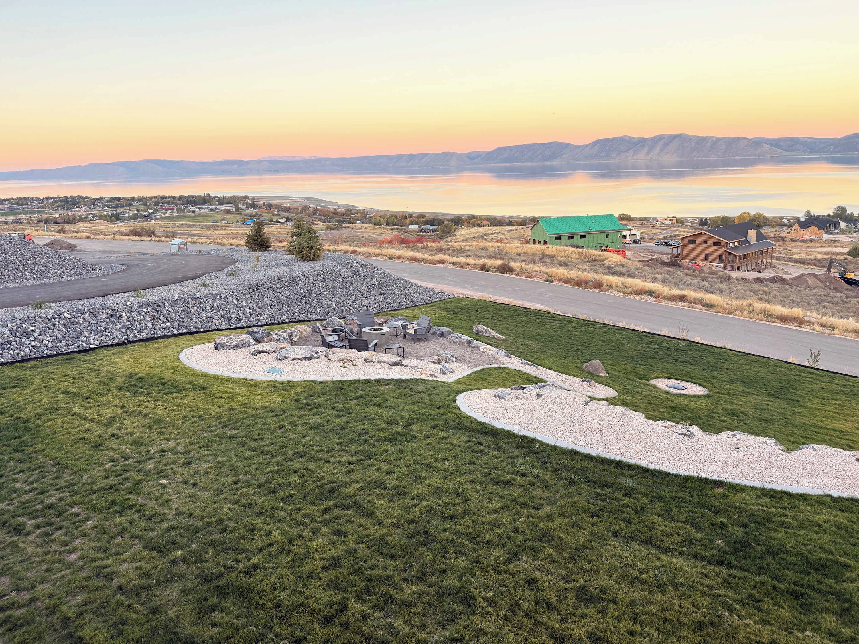 A landscaped area with a circular seating arrangement, a paved path, and a view of a lake and mountains in the distance.