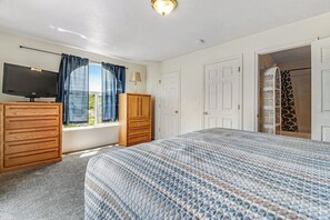 Une chambre à coucher avec un lit, une télévision, une armoire et une fenêtre avec des rideaux.
