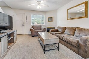 Un salon comprenant un canapé, un fauteuil, une table basse, un téléviseur et un ventilateur de plafond.
