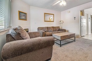 A living room with a brown sofa, a wooden coffee table, and a ceiling fan. - Lakeview Condo 941-1 (Garden City)