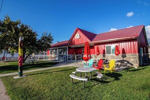 A red building with a sloped roof, outdoor seating with red umbrellas, and a picnic table. - Lakeview Condo 941-1 (Garden City)
