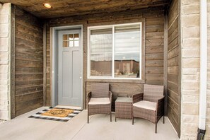Eine Holzfassade mit einer grauen Tür, zwei Korbstühlen und einem kleinen Tisch.