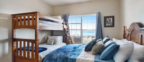 A bedroom with bunk beds, a ceiling fan, a large window with curtains, and a framed picture on the wall.