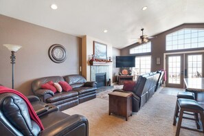 A spacious living room with a fireplace, a television, and a large window. - The Lakehouse - Lake Views, Sleeps 31, Dogs OK (Garden City)
