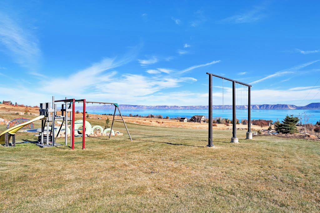 An outdoor playground with swings and a slide, set against a backdrop of mountains and a clear sky.
