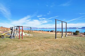 An outdoor playground with swings and a slide, set against a backdrop of mountains and a clear sky. - The Lakehouse - Lake Views, Sleeps 31, Dogs OK (Garden City)