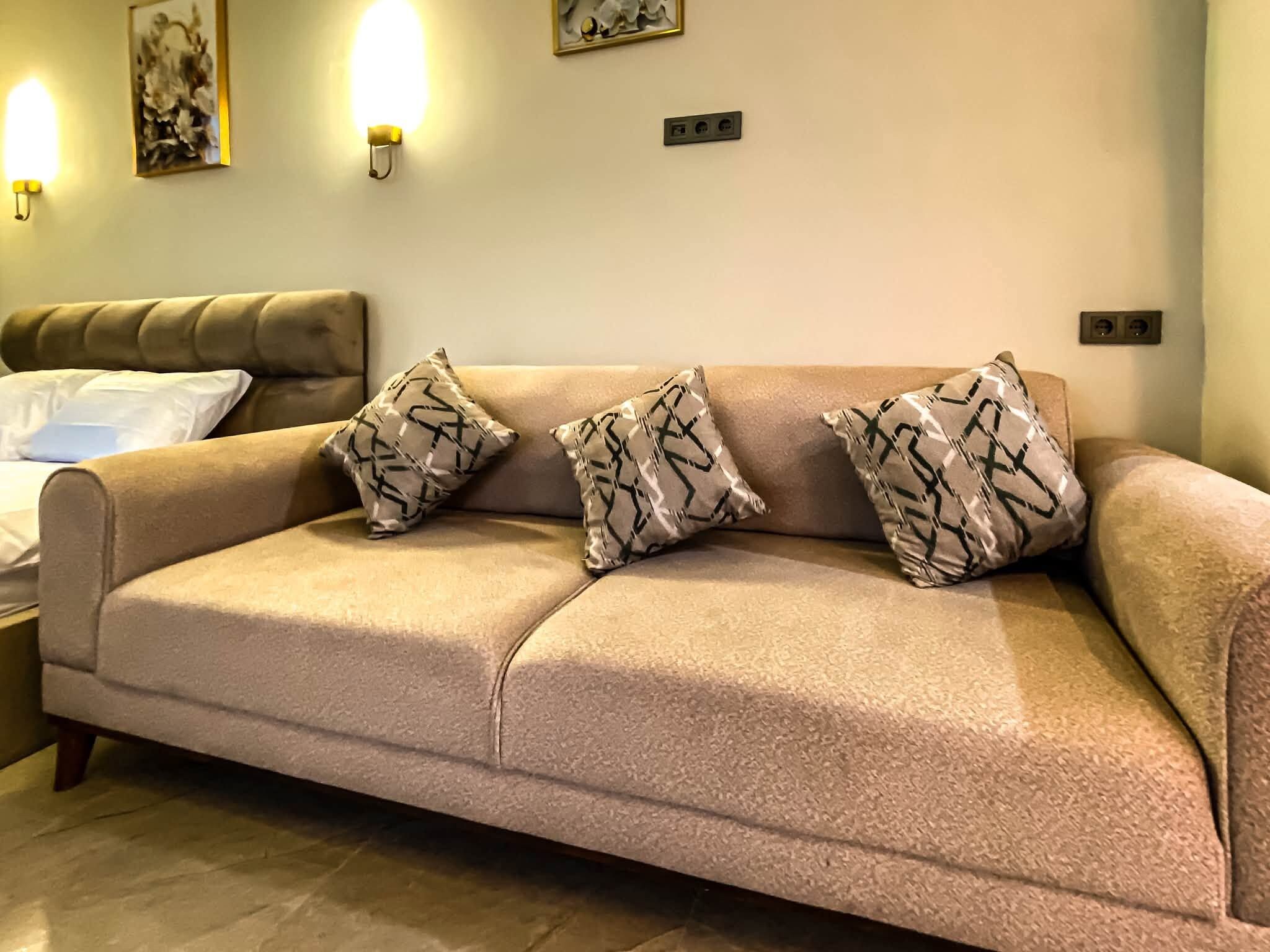Un canapé beige agrémenté de trois coussins à motifs, une table de chevet et des appliques murales.
