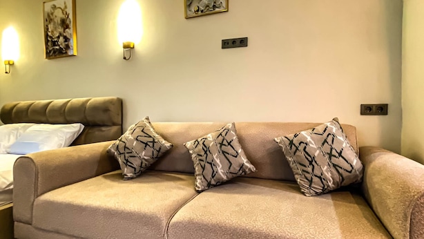 A beige sofa with three patterned cushions, a bedside table, and wall-mounted light fixtures.