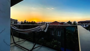 A balcony with a hammock, overlooking a cityscape during sunset.