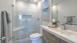 Un baño moderno con ducha envuelta en vidrio, inodoro blanco y tocador con espejo y lavamanos.