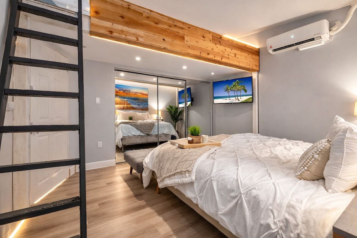 A bedroom with a bed, a wooden ladder, a wall-mounted air conditioner, and a television.