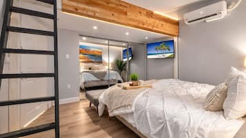 Une chambre à coucher avec un lit, une échelle en bois, un climatiseur fixé au mur et un téléviseur.