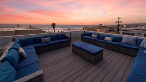 Terraza en la azotea con mobiliario exterior y vistas al océano al atardecer.