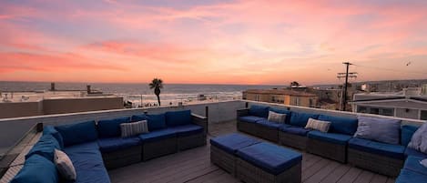 A rooftop terrace with outdoor seating and a view of the ocean at sunset.