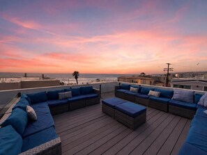 En tagterrasse med udendørs siddepladser og havudsigt i solnedgangen.