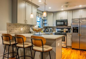A modern kitchen with a central island, bar stools, stainless steel appliances, and pendant lighting.