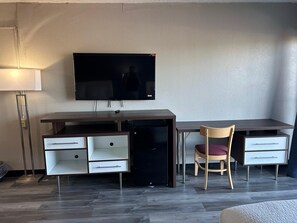 A room with a desk, chair, TV, and a lamp.