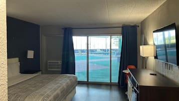 A hotel room with a bed, a desk, a TV, and a view of a pool and tennis court.