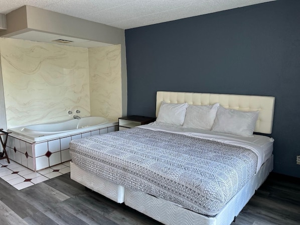 A bedroom with a large bed, a separate bathroom with a bathtub, and a wooden floor.