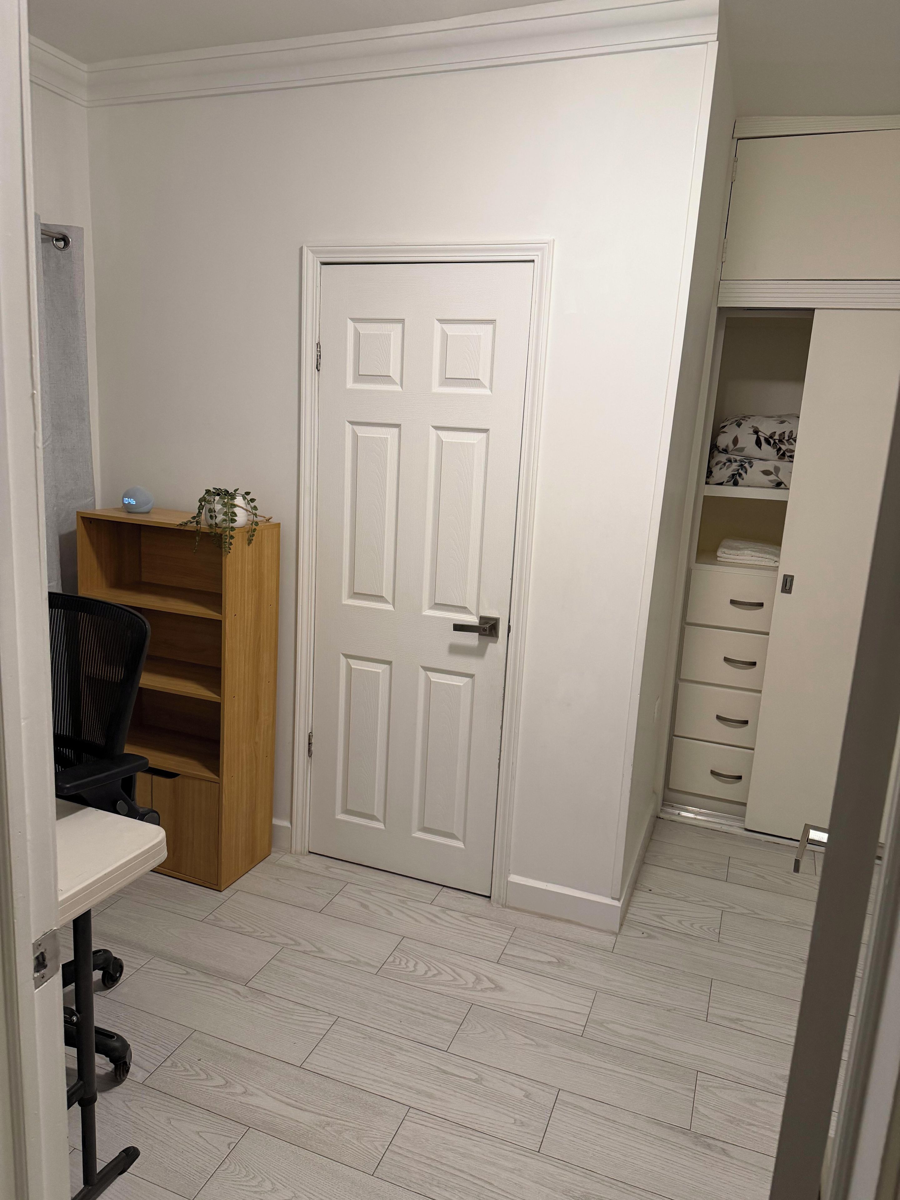 Een kamer met een witte deur, een houten stoel, een bureau en een boekenkast.