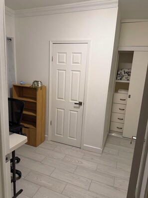 A room with a white door, a wooden chair, a desk, and a shelving unit.